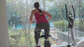 Sportliches Reiten der jungen Frau auf Hometrainer an der Turnhalle in der Zeitlupe, hintere Ansicht stock video footage Sportliches Reiten der jungen Frau auf Hometrainer an der Turnhalle in der Zeitlupe, hintere Ansicht stock video footage