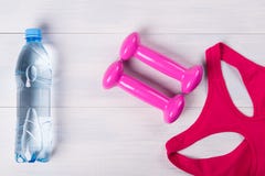 Sportswear γυναικών, με τους ρόδινους αλτήρες, σε ένα ελαφρύ ξύλινο πάτωμα, και ένα μπουκάλι νερό Στοκ Εικόνες Sportswear γυναικών, με τους ρόδινους αλτήρες, σε ένα ελαφρύ ξύλινο πάτωμα, και ένα μπουκάλι νερό Στοκ Εικόνες