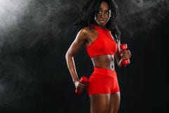 Sporty fit black skin woman in red sportswear, athlete with dumbbells makes fitness exercising on dark background. royalty free stock image Sporty fit black skin woman in red sportswear, athlete with dumbbells makes fitness exercising on dark background. royalty free stock image