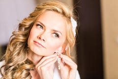 Sposa bionda elegante che mette sul primo piano degli orecchini, preparante per le nozze fotografia stock libera da diritti Sposa bionda elegante che mette sul primo piano degli orecchini, preparante per le nozze fotografia stock libera da diritti