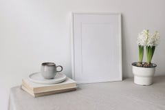 Spring breakfast still life scene. Cup of coffee, books. Empty white picture frame mockup. Beige linen tablecloth
