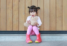 St?enden av den gulliga lilla flickan sitter och krama Teddy Bear mot den wood plankav?ggen arkivbild St?enden av den gulliga lilla flickan sitter och krama Teddy Bear mot den wood plankav?ggen arkivbild