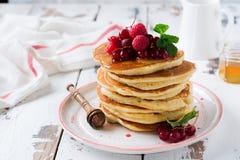 Stack of homemade little pancakes with honey, fresh raspberries and red currants on an old light wooden background. royalty free stock photography Stack of homemade little pancakes with honey, fresh raspberries and red currants on an old light wooden background. royalty free stock photography