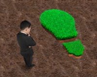 Standing businessman pondering over green grass of light bulb stock image Standing businessman pondering over green grass of light bulb stock image