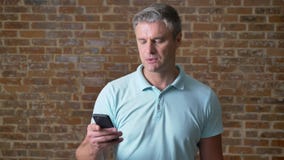 Starszy caucasian mężczyzna skupia się na pisać na maszynie w telefonie komórkowym spokojnie i pozycji w czerwony pracowniany sam zbiory wideo Starszy caucasian mężczyzna skupia się na pisać na maszynie w telefonie komórkowym spokojnie i pozycji w czerwony pracowniany sam zbiory wideo