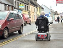 Stary dżentelmen Jedzie Elektrycznego krzesła footpath wewnątrz zdjęcie stock Stary dżentelmen Jedzie Elektrycznego krzesła footpath wewnątrz zdjęcie stock