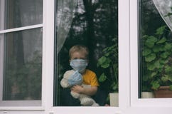 Stay at home quarantine for coronavirus pandemic prevention. Sad child and his teddy bear both in protective medical masks sits on