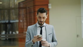 Stedicam tiró del hombre de negocios alegre que hablaba con smartphone y que caminaba en pasillo moderno de la oficina Stedicam tiró del hombre de negocios alegre que hablaba con smartphone y que caminaba en pasillo moderno de la oficina