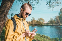 Stile di vita all'aperto di estate del telefono cellulare maschio di tocco dei pantaloni a vita bassa in parco immagine stock libera da diritti Stile di vita all'aperto di estate del telefono cellulare maschio di tocco dei pantaloni a vita bassa in parco immagine stock libera da diritti