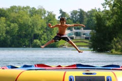 Stilig gullig pojkebanhoppning på en vattentrampolin som svävar i en sjö i Michigan under sommar arkivbilder Stilig gullig pojkebanhoppning på en vattentrampolin som svävar i en sjö i Michigan under sommar arkivbilder