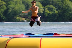 Stilig gullig pojkebanhoppning på en vattentrampolin som svävar i en sjö i Michigan under sommar arkivfoton Stilig gullig pojkebanhoppning på en vattentrampolin som svävar i en sjö i Michigan under sommar arkivfoton