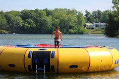 Stilig gullig pojkebanhoppning på en vattentrampolin som svävar i en sjö i Michigan under sommar arkivbild Stilig gullig pojkebanhoppning på en vattentrampolin som svävar i en sjö i Michigan under sommar arkivbild