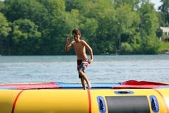 Stilig gullig pojkebanhoppning på en vattentrampolin som svävar i en sjö i Michigan under sommar arkivfoton Stilig gullig pojkebanhoppning på en vattentrampolin som svävar i en sjö i Michigan under sommar arkivfoton