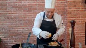 Stilig manlig likformig för iklädd vit för kock som dekorerar paella och ser le för kamera lager videofilmer Stilig manlig likformig för iklädd vit för kock som dekorerar paella och ser le för kamera lager videofilmer