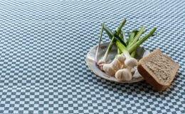Stillleben mit jungem Knoblauch auf Weinleseplatte mit einem Frieden des Weißbrots, Nahaufnahme lizenzfreies stockfoto Stillleben mit jungem Knoblauch auf Weinleseplatte mit einem Frieden des Weißbrots, Nahaufnahme lizenzfreies stockfoto