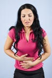 Stomach pain. Big stomach pain of young brunette woman in pink t-shirt over blue background,she standing with both hands on stomach hurting,same series in Stomach pain. Big stomach pain of young brunette woman in pink t-shirt over blue background,she standing with both hands on stomach hurting,same series in
