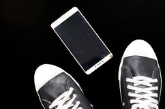 Stopa w łamającym telefonie na czarnym tle i sneakers obrazy royalty free Stopa w łamającym telefonie na czarnym tle i sneakers obrazy royalty free