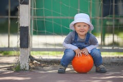 Street portrait of the cute little boy playing with the orange ball