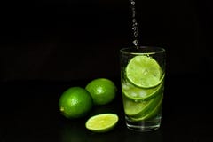 Strom gießt in ein Glas des kalten Getränks mit Eis und frischen reifen Scheibengrünkalken auf schwarzem Hintergrund stockfoto Strom gießt in ein Glas des kalten Getränks mit Eis und frischen reifen Scheibengrünkalken auf schwarzem Hintergrund stockfoto