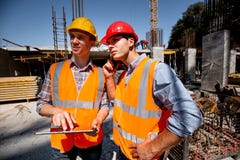 Structural engineer and architect dressed in orange work vests and hard bats discuss the construction process by the royalty free stock photography Structural engineer and architect dressed in orange work vests and hard bats discuss the construction process by the royalty free stock photography