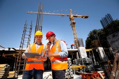 Structural engineer and architect dressed in orange work vests and hard hats discuss the construction process by the stock image Structural engineer and architect dressed in orange work vests and hard hats discuss the construction process by the stock image