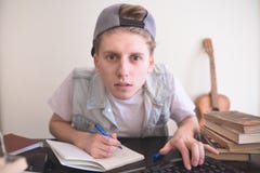 Student sits at a computer near the books, looks at the monitor and writes in a notebook stock image Student sits at a computer near the books, looks at the monitor and writes in a notebook stock image