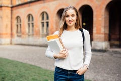 Studente di college femminile astuto con la borsa e libri sulla città universitaria all'aperto immagine stock libera da diritti Studente di college femminile astuto con la borsa e libri sulla città universitaria all'aperto immagine stock libera da diritti