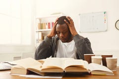 Studente maschio nero che studia alla tavola in pieno dei libri fotografia stock libera da diritti Studente maschio nero che studia alla tavola in pieno dei libri fotografia stock libera da diritti