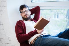 Studente in vetri che si siedono sul davanzale e sulla lettura della finestra fotografia stock libera da diritti Studente in vetri che si siedono sul davanzale e sulla lettura della finestra fotografia stock libera da diritti