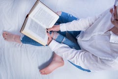 Studentflickaläsebok i hemtrevlig säng- och rymmabok på ben med kal fot arkivfoto Studentflickaläsebok i hemtrevlig säng- och rymmabok på ben med kal fot arkivfoto