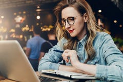 Studentflickan i moderiktiga exponeringsglas sitter i kafé framme av datoren, bildande webinar för bärbar datorklockor utbildning arkivbilder Studentflickan i moderiktiga exponeringsglas sitter i kafé framme av datoren, bildande webinar för bärbar datorklockor utbildning arkivbilder