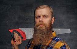Bearded carpenter dressed in a plaid shirt holds handsaw. Royalty Free Stock Photography Bearded carpenter dressed in a plaid shirt holds handsaw. Royalty Free Stock Photography