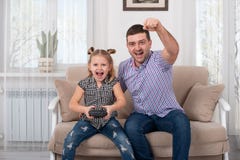 Studio shot of a little girl and her dad sitting on the sofa at home with the joystick and together emotionally playing a game royalty free stock photos Studio shot of a little girl and her dad sitting on the sofa at home with the joystick and together emotionally playing a game royalty free stock photos