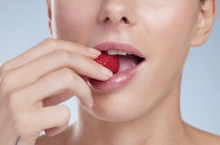Biting into goodness. Studio shot of an unrecognizable young woman biting into a strawberry against a grey background.