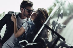 Stylish young couple hugging and kissing on motorcycle outdoors