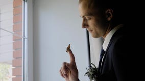 Stylish young guy puts on a jacket standing on the balcony. Beautiful view from the room through the curtain behind the guy. stock video footage Stylish young guy puts on a jacket standing on the balcony. Beautiful view from the room through the curtain behind the guy. stock video footage
