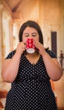 Stäng sig upp av den nätta feta kvinnan i en härlig klänning, den dra koppen av coffe i en suddig bakgrund royaltyfria foton Stäng sig upp av den nätta feta kvinnan i en härlig klänning, den dra koppen av coffe i en suddig bakgrund royaltyfria foton