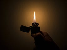 Stäng sig upp av en svart tändare som rymms av en hand, med att bedöva den orange och blåa flamman fotografering för bildbyråer Stäng sig upp av en svart tändare som rymms av en hand, med att bedöva den orange och blåa flamman fotografering för bildbyråer