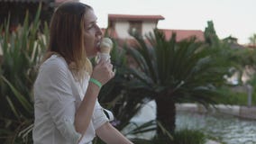 Stående av den härliga positiva unga kvinnan som äter glass på bakgrund av palmträd lager videofilmer Stående av den härliga positiva unga kvinnan som äter glass på bakgrund av palmträd lager videofilmer