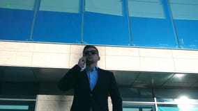 Stående av den unga affärsmannen i solglasögon som talar på telefonen som är utomhus- nära kontor Stäng sig upp av stilig affärsm stock video Stående av den unga affärsmannen i solglasögon som talar på telefonen som är utomhus- nära kontor Stäng sig upp av stilig affärsm stock video