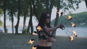 Stående av den unga härliga kvinnan i maskeringen som framme utför en show med flammaanseende på flodstrand av träd skillful arkivfilmer Stående av den unga härliga kvinnan i maskeringen som framme utför en show med flammaanseende på flodstrand av träd skillful arkivfilmer