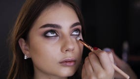 Stående av den unga kvinnan medan makeupögon i kosmetisk studio Makeupkonstnär som använder borsten för att applicera ljus ögonsk stock video Stående av den unga kvinnan medan makeupögon i kosmetisk studio Makeupkonstnär som använder borsten för att applicera ljus ögonsk stock video