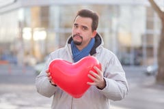 Stående av en hipsterman med ett skägg som poserar med en röd ballong för lufthjärtaform i stadsgata med mjukt framsidauttryck arkivfoton Stående av en hipsterman med ett skägg som poserar med en röd ballong för lufthjärtaform i stadsgata med mjukt framsidauttryck arkivfoton