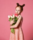 Stående av en härlig ung flicka i klänningen som rymmer den stora buketten av iriers och tulpan som isoleras över rosa bakgrund arkivbild Stående av en härlig ung flicka i klänningen som rymmer den stora buketten av iriers och tulpan som isoleras över rosa bakgrund arkivbild