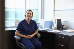 Stående av sjuksköterskan Wearing Scrubs Sitting på skrivbordet i regeringsställning arkivfoton Stående av sjuksköterskan Wearing Scrubs Sitting på skrivbordet i regeringsställning arkivfoton