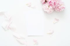 Summer feminine wedding or birthday flat lay composition with peonies floral bouquet and silk ribbon. Blank paper card