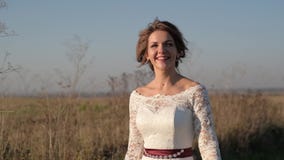 On a sunny day, a woman walks across a field in a white dress against a background of nature. stock footage On a sunny day, a woman walks across a field in a white dress against a background of nature. stock footage