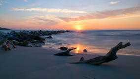 Sunrise seen from the sand, stones leaving the sea and a log buried in sand on the shore of the Mediterranean Sea royalty free stock photo Sunrise seen from the sand, stones leaving the sea and a log buried in sand on the shore of the Mediterranean Sea royalty free stock photo