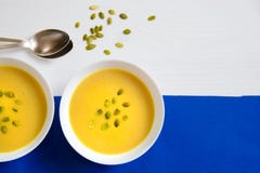 Suppe des Kürbises und der Sonnenblumensamen in einer weißen Platte mit silbernen Löffeln auf einem hellen Hintergrund Das Konzep lizenzfreie stockfotos Suppe des Kürbises und der Sonnenblumensamen in einer weißen Platte mit silbernen Löffeln auf einem hellen Hintergrund Das Konzep lizenzfreie stockfotos