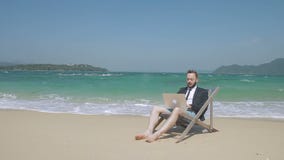 Sur la plage le jeune homme derrière l'ordinateur portable fait des affaires en vacances banque de vidéos Sur la plage le jeune homme derrière l'ordinateur portable fait des affaires en vacances banque de vidéos